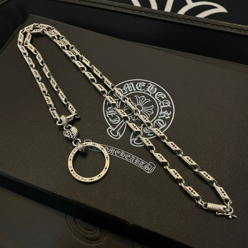 Silver tone chain necklace set on a black box surface, with round hoop pendant.