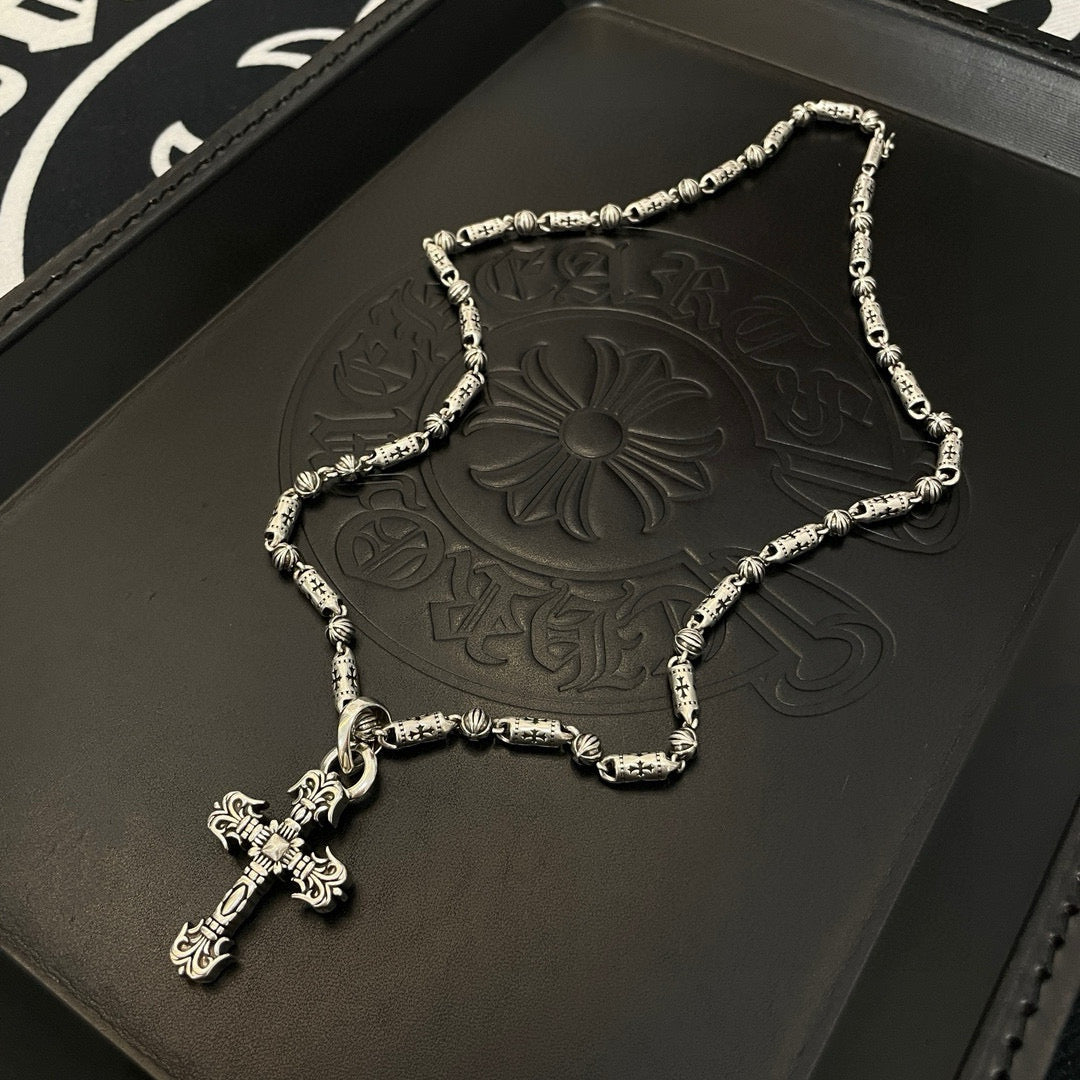 Silver-toned beaded chain cross pendant necklace on black embossed tray