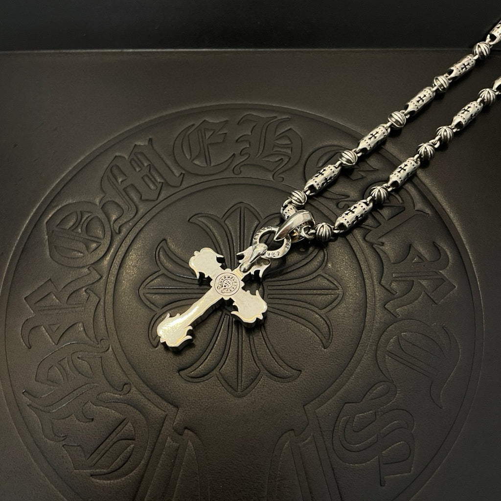 Silver-toned cross pendant necklace with gold-toned center detail on embossed tray