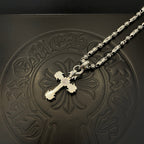 Silver-toned cross pendant necklace with gold-toned center detail on embossed tray