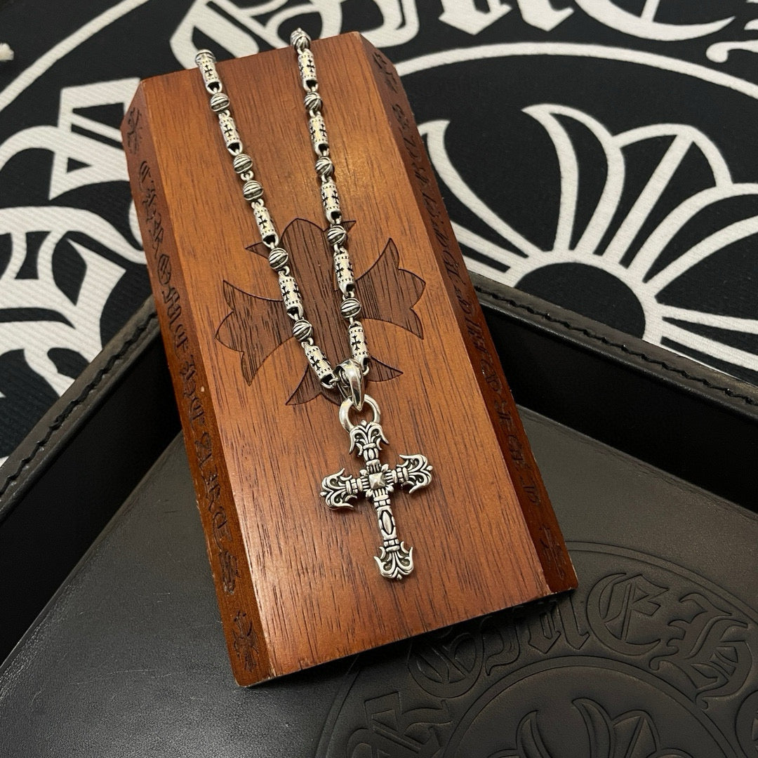 Silver-toned beaded chain cross pendant necklace on brown wooden display box