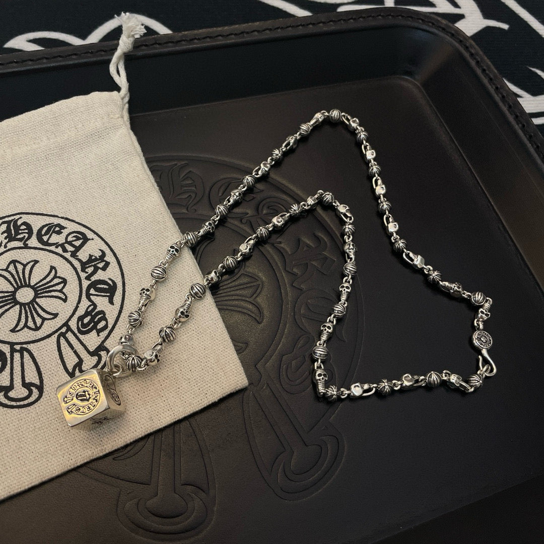 Silver tone chain necklace with round pendant charm on dark tray and pouch