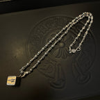 Silver-tone chain necklace with heart-shaped pendant, laid on a patterned black surface