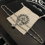 Silver-tone chain necklace with square and heart pendants, resting on a fabric pouch