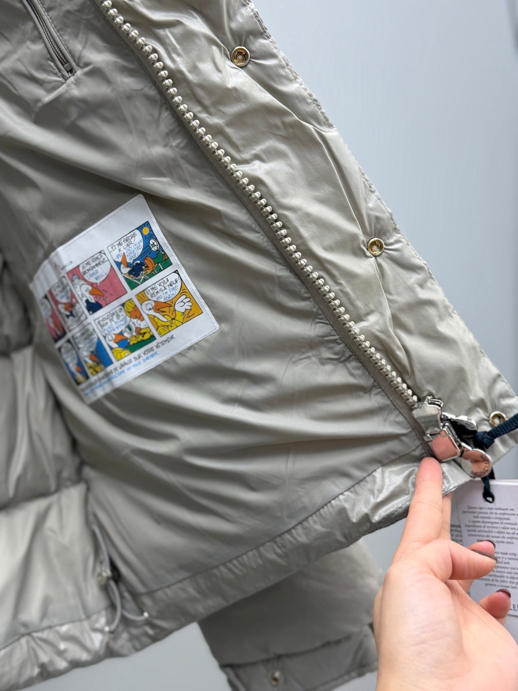 Light gray puffer jacket with zipper pull, gold buttons, and fabric tag patch