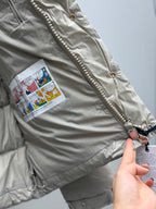 Light gray puffer jacket with zipper pull, gold buttons, and fabric tag patch