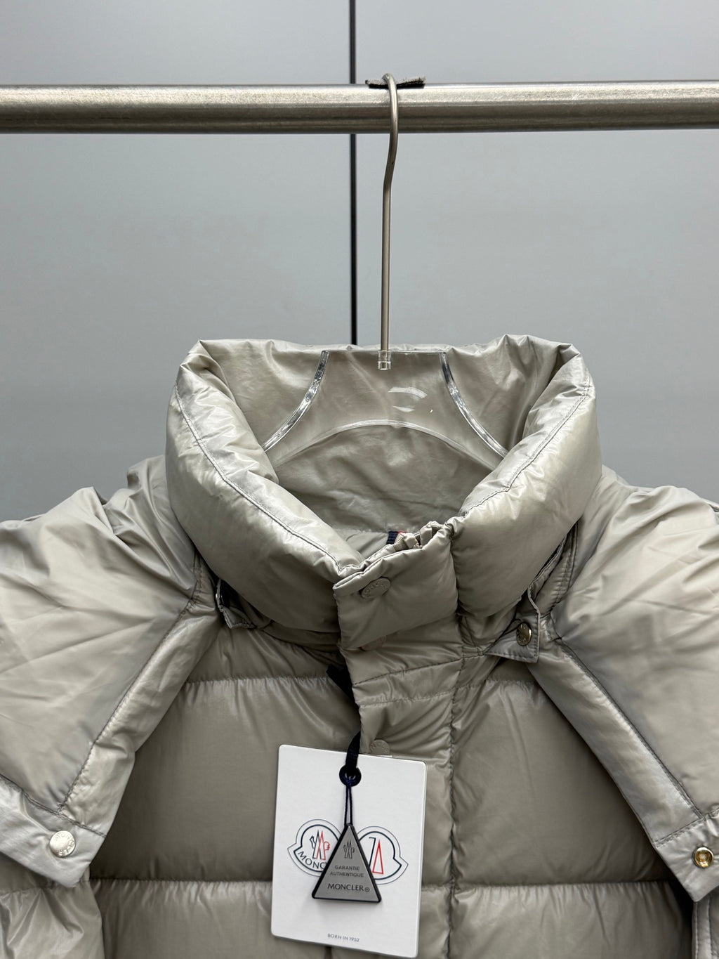 Light gray hooded puffer jacket close-up with front snap buttons and tag