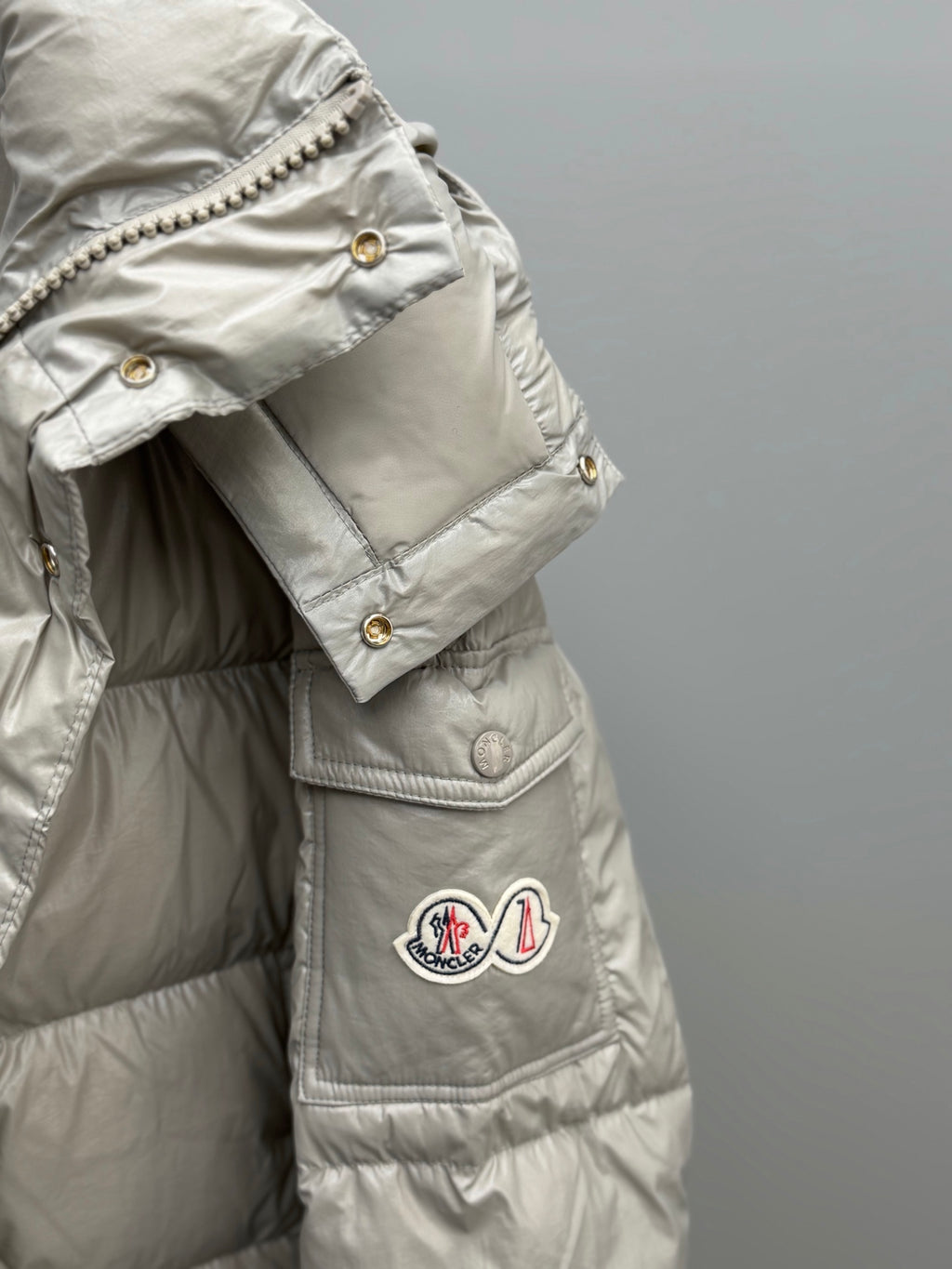 Light gray puffer jacket sleeve and chest pocket with snap buttons and logo patch