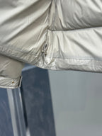 Light gray puffer jacket hem detail with drawstring toggle and stitched seam