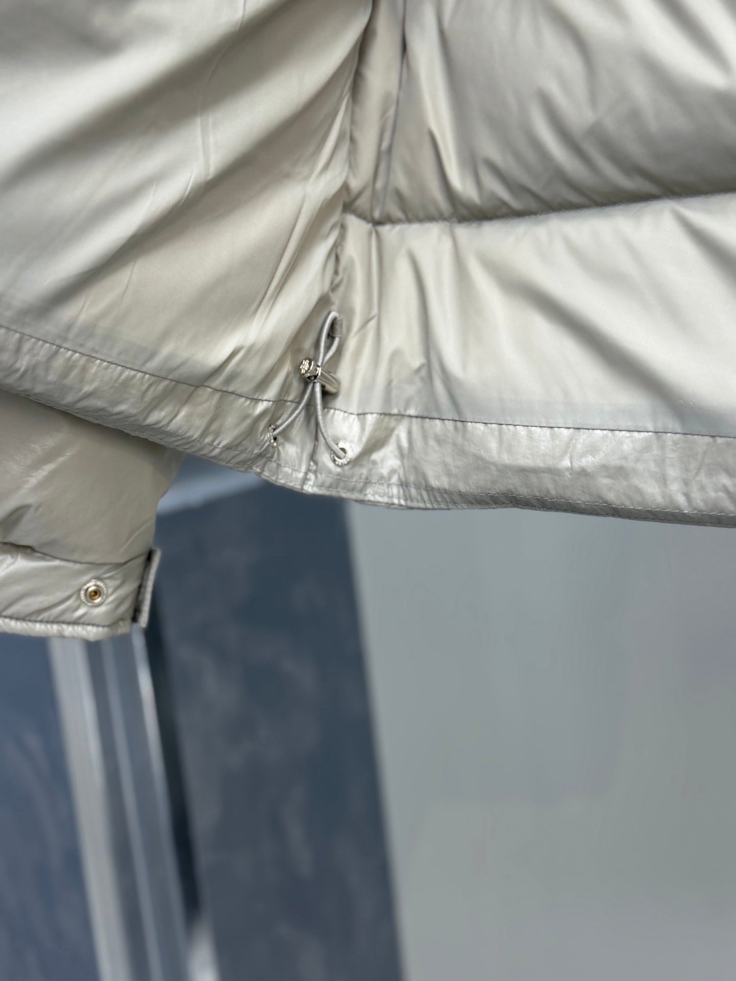 Light gray puffer jacket hem detail with drawstring toggle and stitched seam