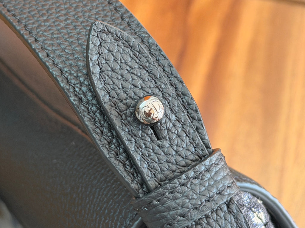 Black Dior leather bag strap end with circular logo snap detail.