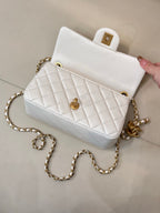 White quilted Chanel flap bag with gold chain strap, top handle, and CC button.