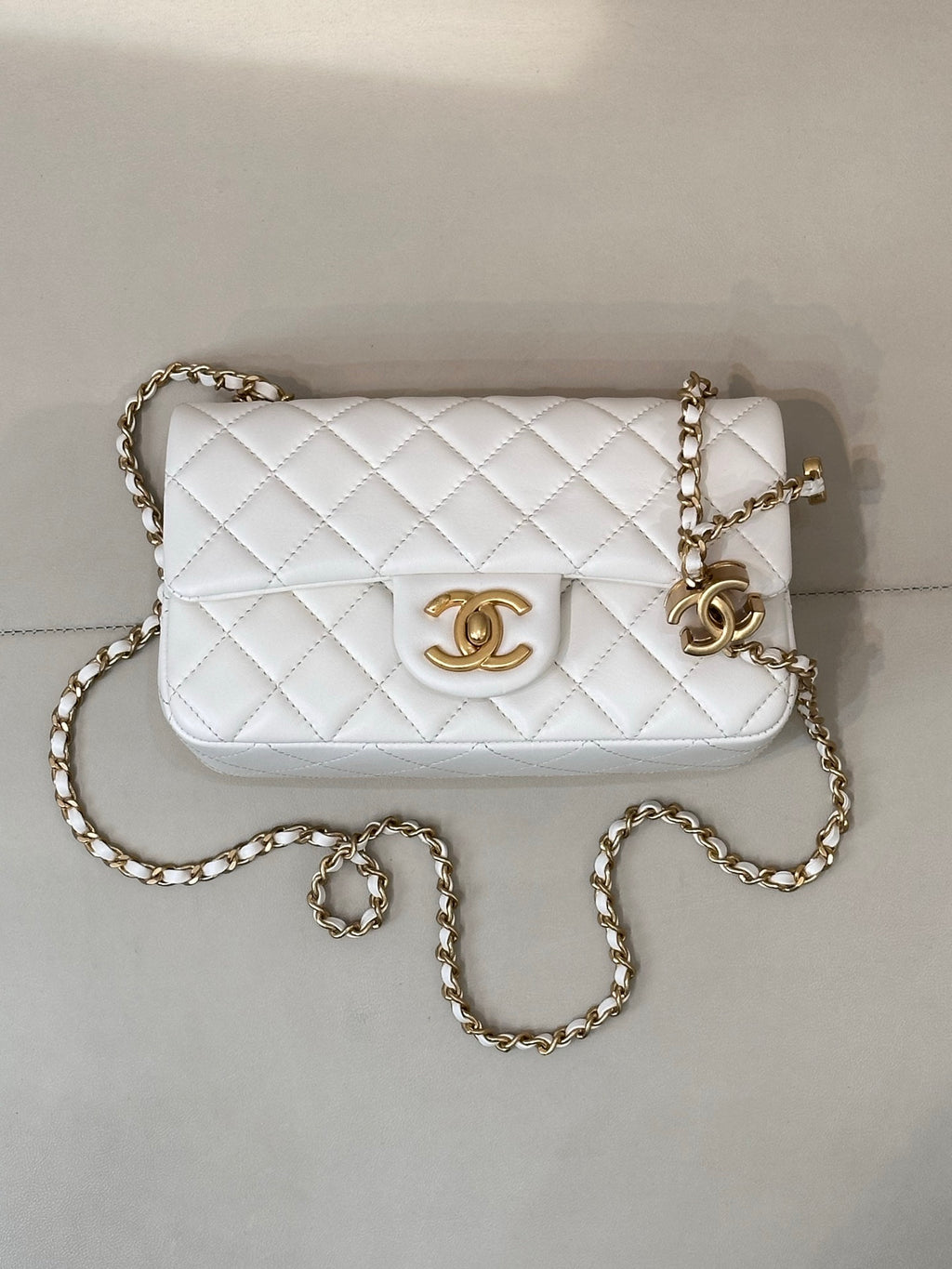 White quilted Chanel shoulder bag with gold chain strap and CC logo front panel.