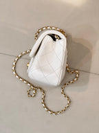 White quilted Chanel bag with gold chain strap, small top handle, and quilted pattern.