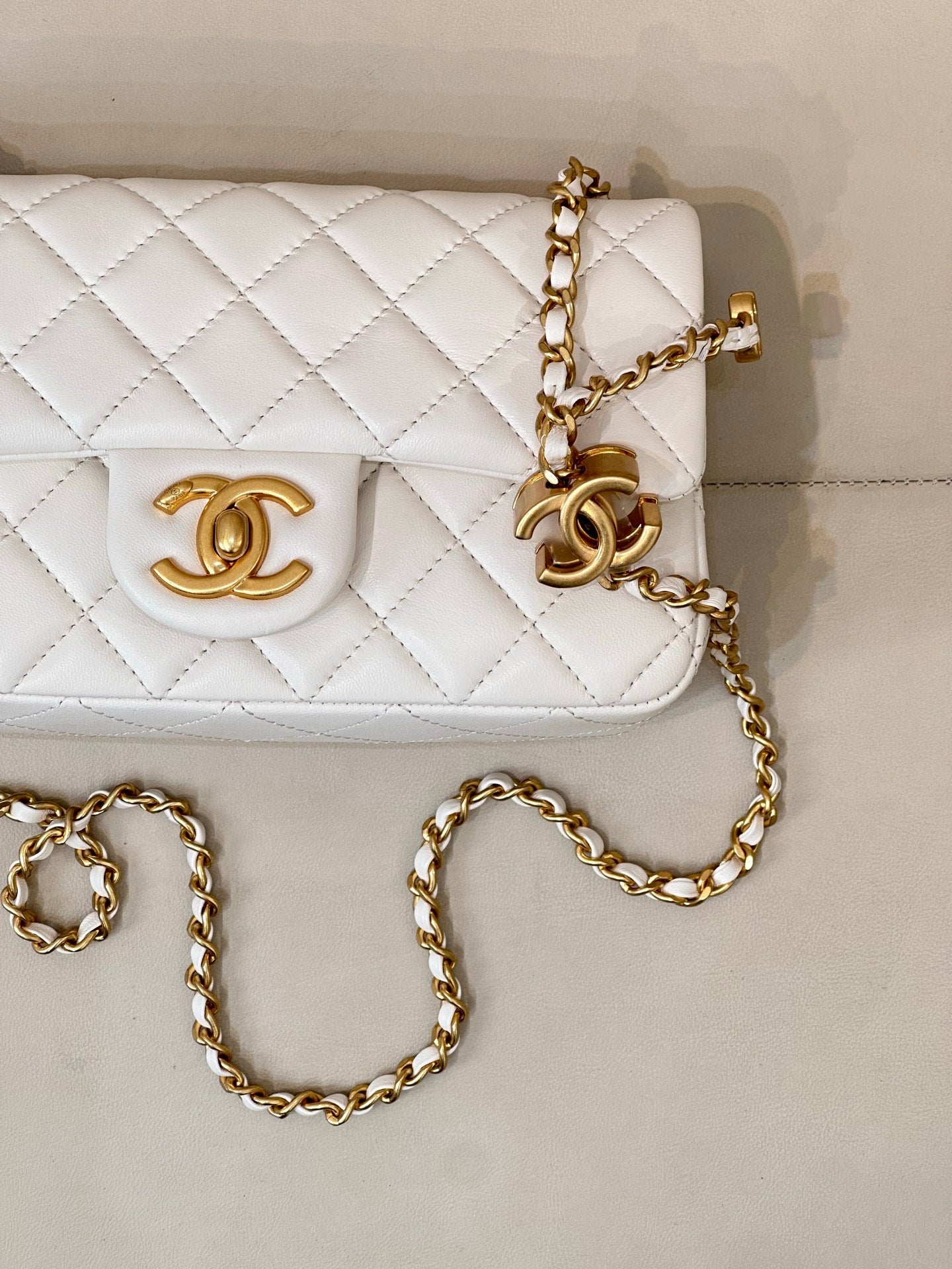 Close-up of white quilted Chanel flap bag with gold CC logo and chain detail.