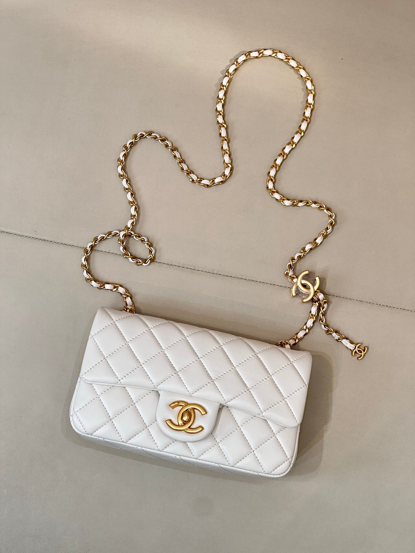 White quilted Chanel flap bag with gold-tone chain strap and CC emblem on front.