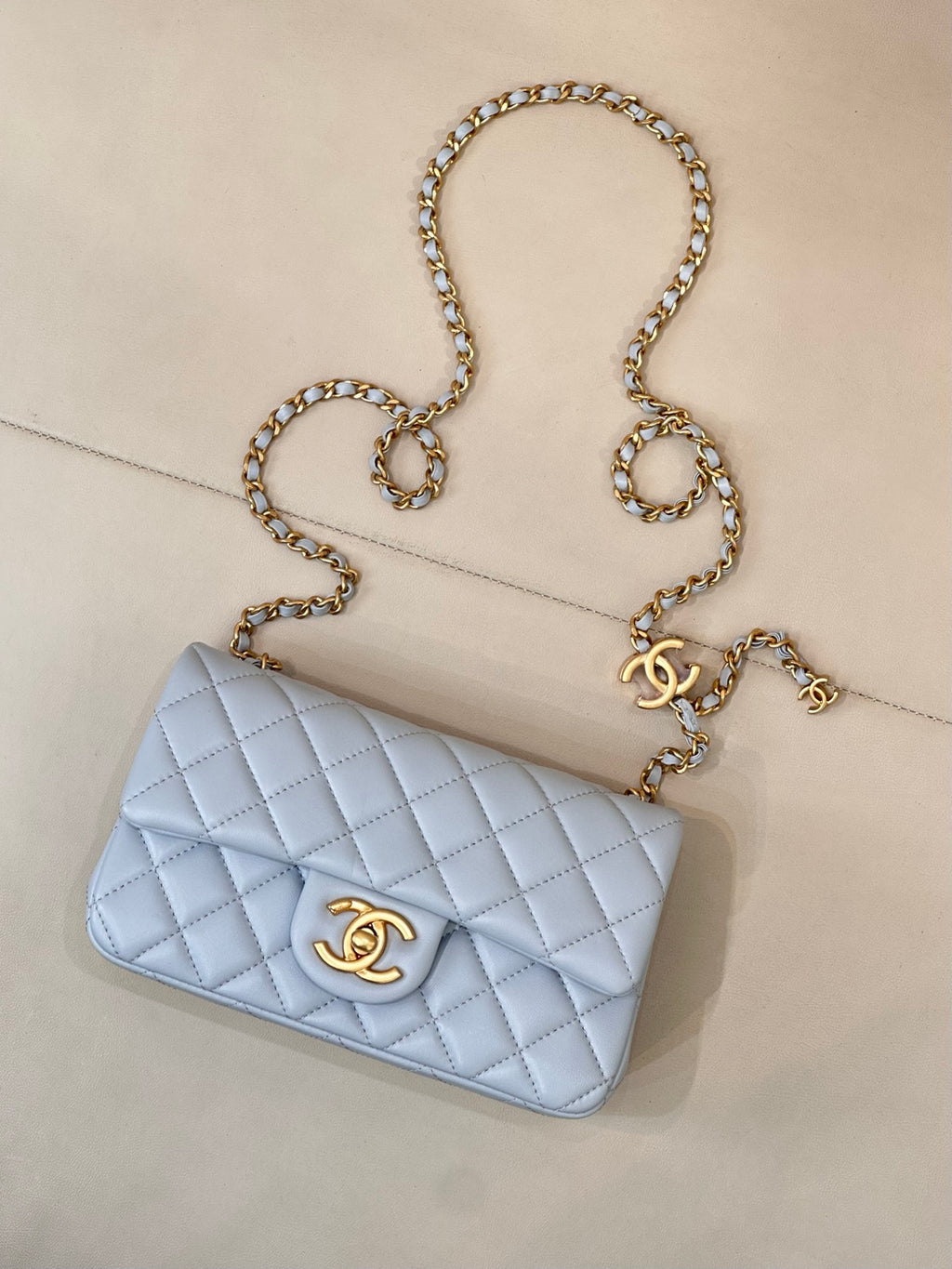 Light blue quilted shoulder bag with gold chain strap and gold logo on flap
