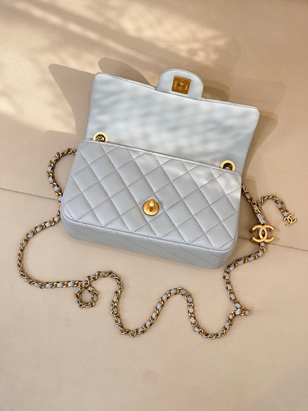 Light blue quilted flap bag with gold chain and gold logo front, open top view