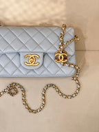 Close view of light blue quilted flap bag with gold logo and gold chain hardware