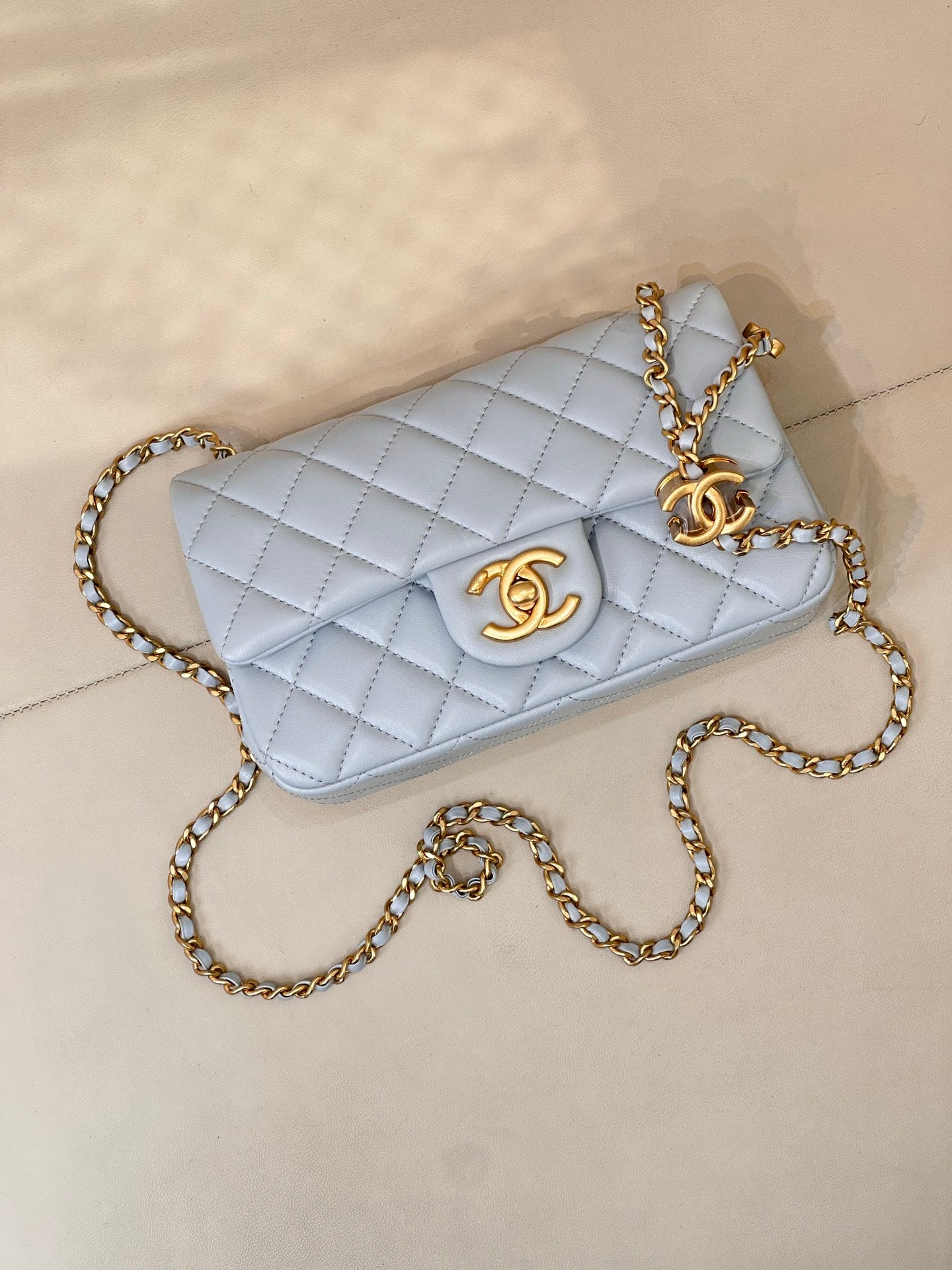 Light blue quilted crossbody bag with gold chain strap and gold logo on front