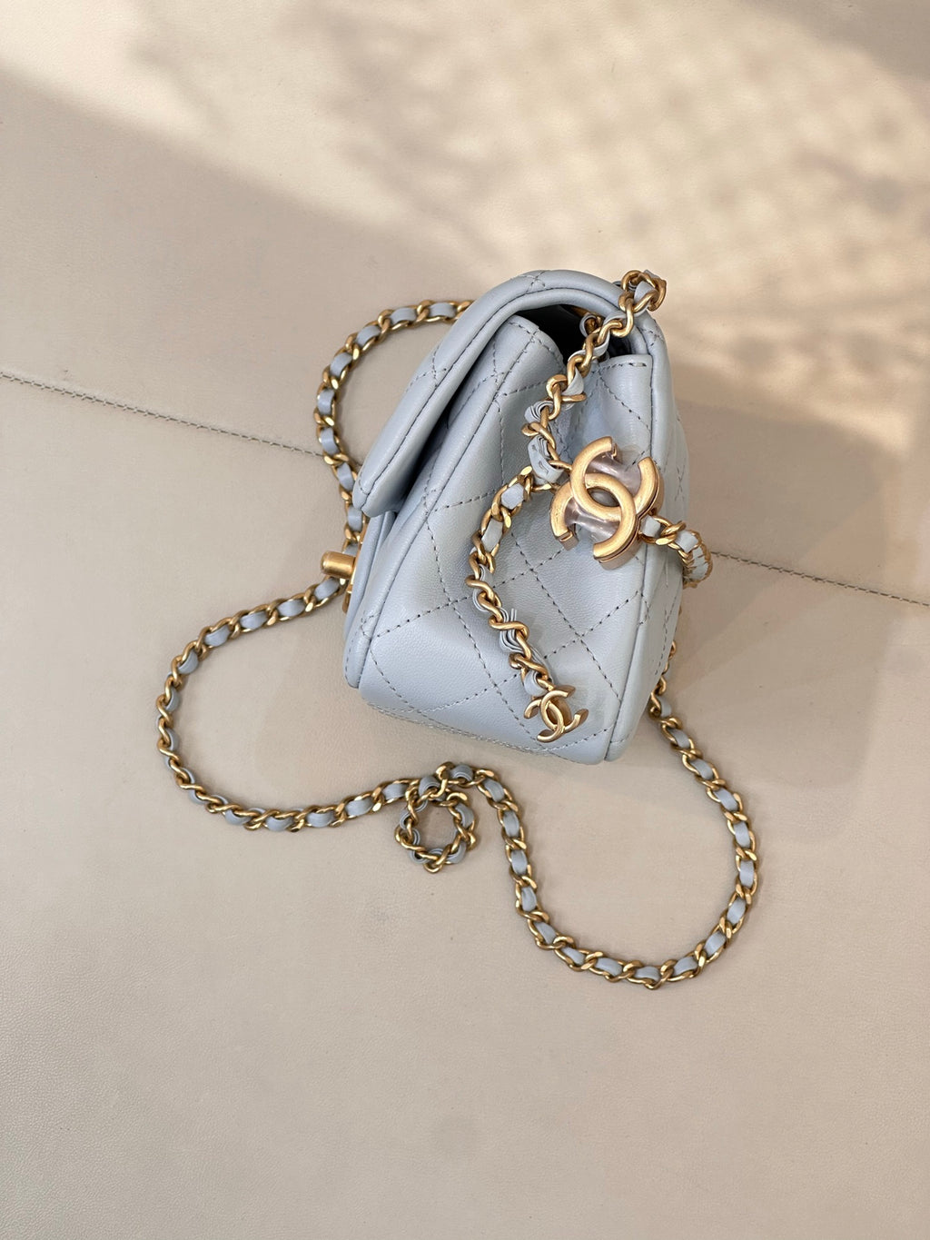 Light blue quilted mini bag with gold chain strap and circular gold logo detail