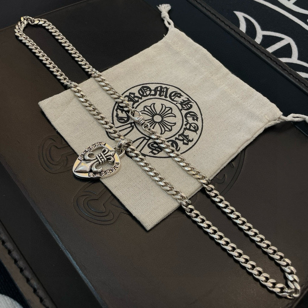 Silver-tone chain necklace with Chrome Hearts heart pendant laid on a cloth pouch