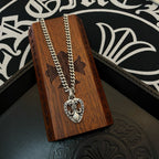 Silver-tone chain necklace with Chrome Hearts heart pendant on a wooden box