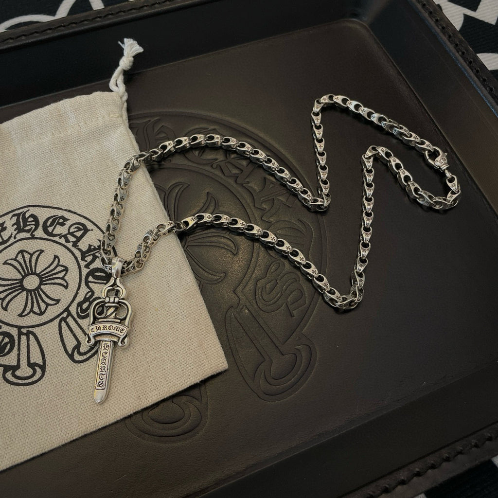 Silver-tone necklace with cross-dagger charm and oval chain beside pouch