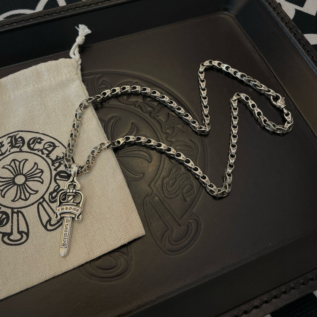 Silver-tone necklace with cross-dagger charm and oval chain beside pouch