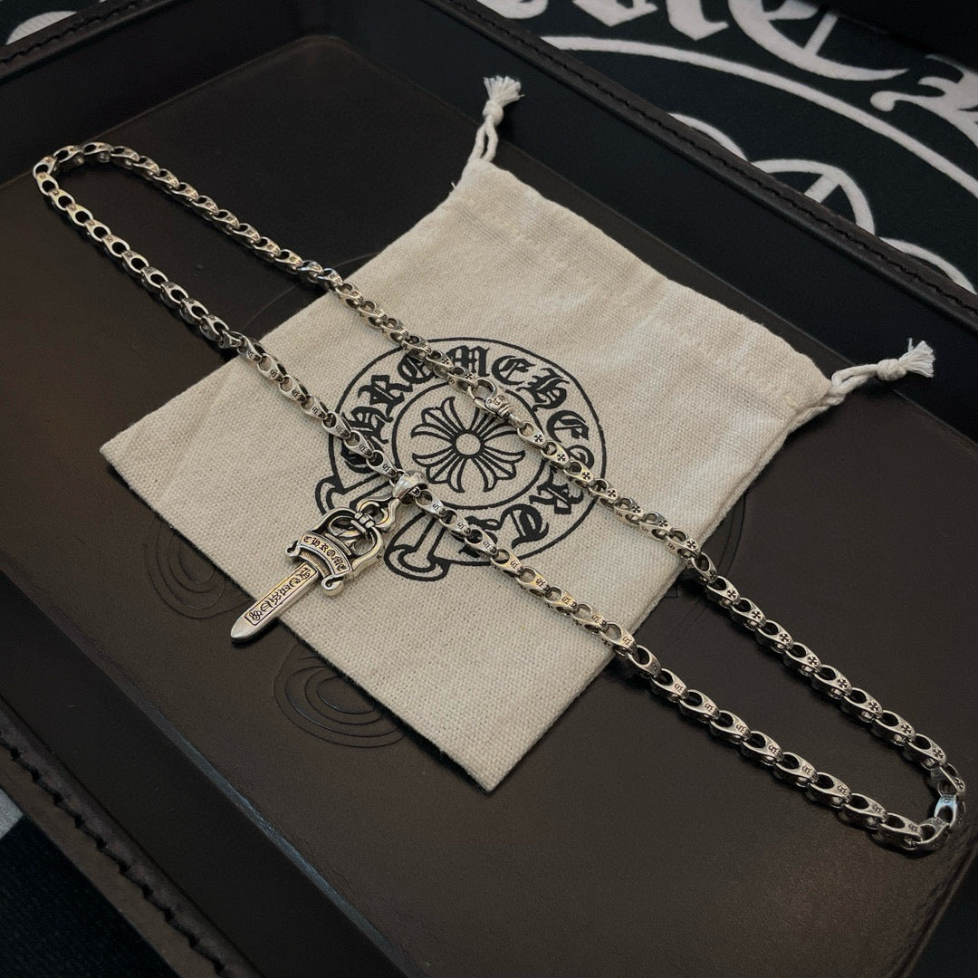 Silver-tone chain necklace with cross dagger pendant on drawstring pouch
