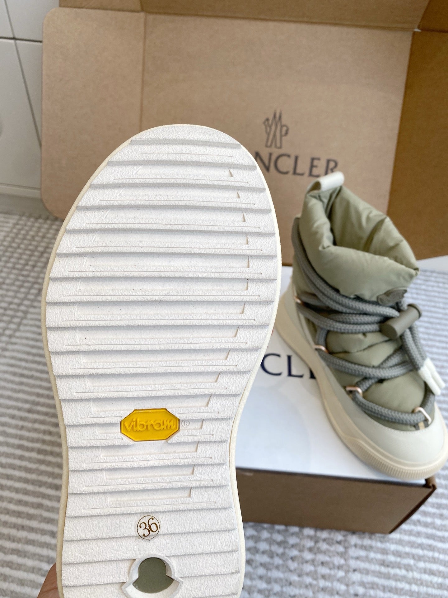Moncler sneaker outsole with white traction tread, sage upper, and lace detail in box