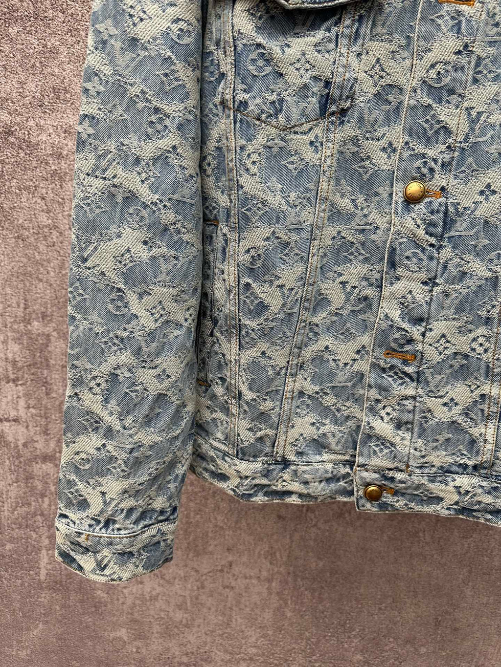 Blue denim jacket close-up with monogram pattern, gold buttons, and side pocket flaps
