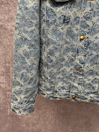 Blue denim jacket close-up with monogram pattern, gold buttons, and side pocket flaps