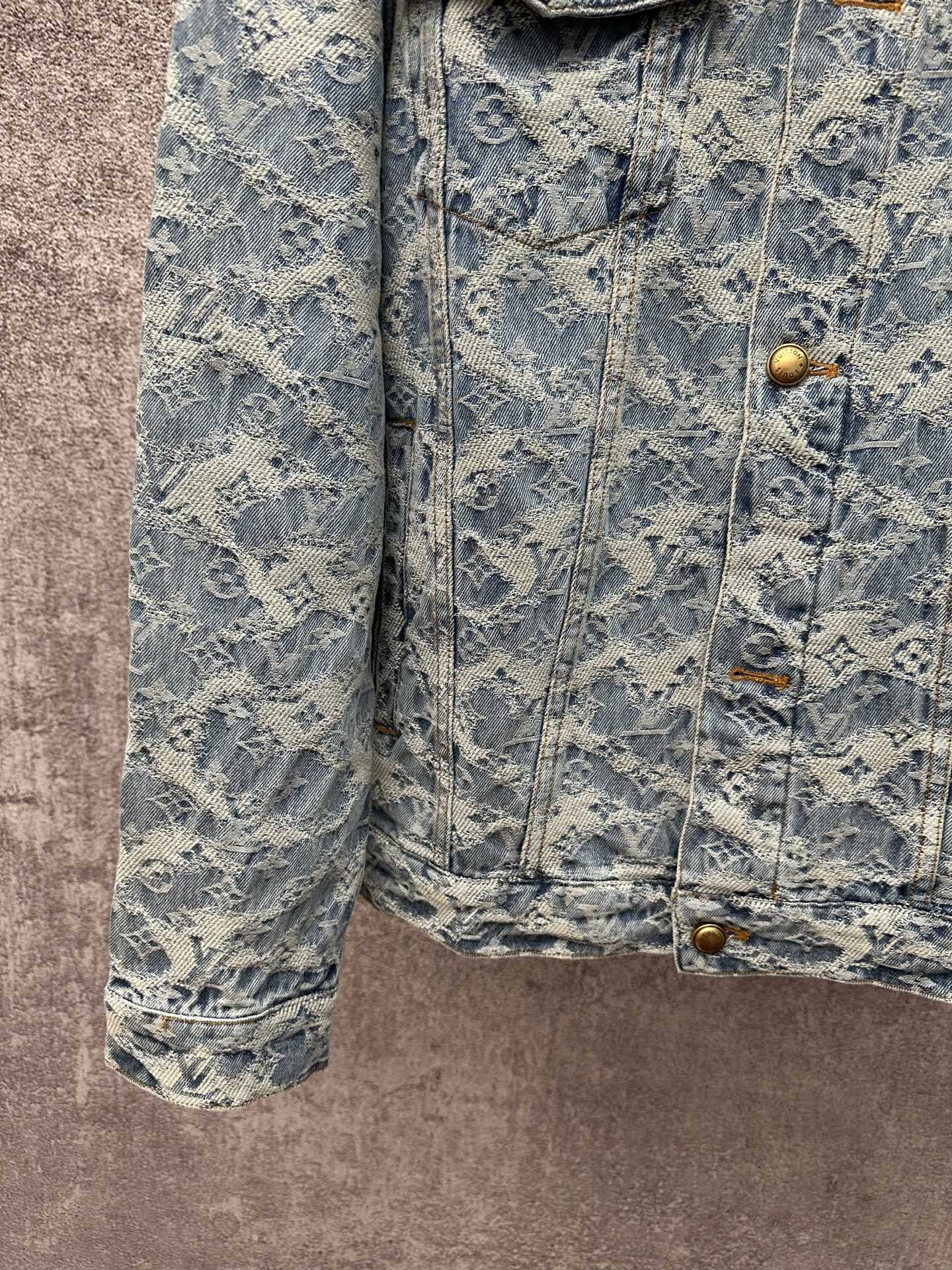 Blue denim jacket close-up with monogram pattern, gold buttons, and side pocket flaps