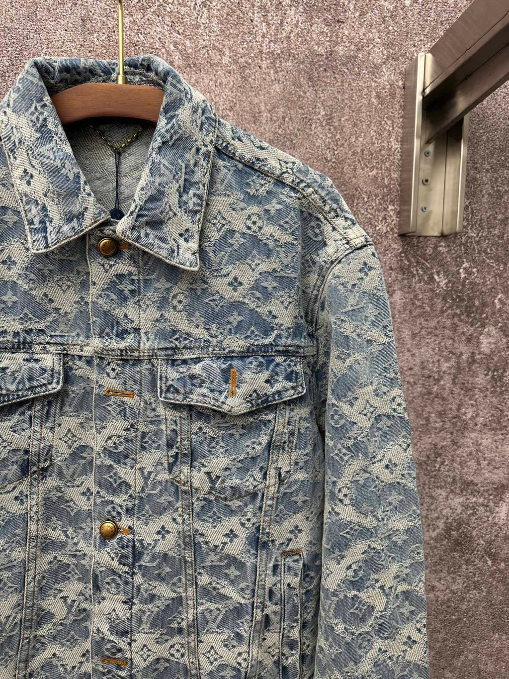 Blue denim jacket close-up with monogram pattern, pointed collar, and chest flap pockets