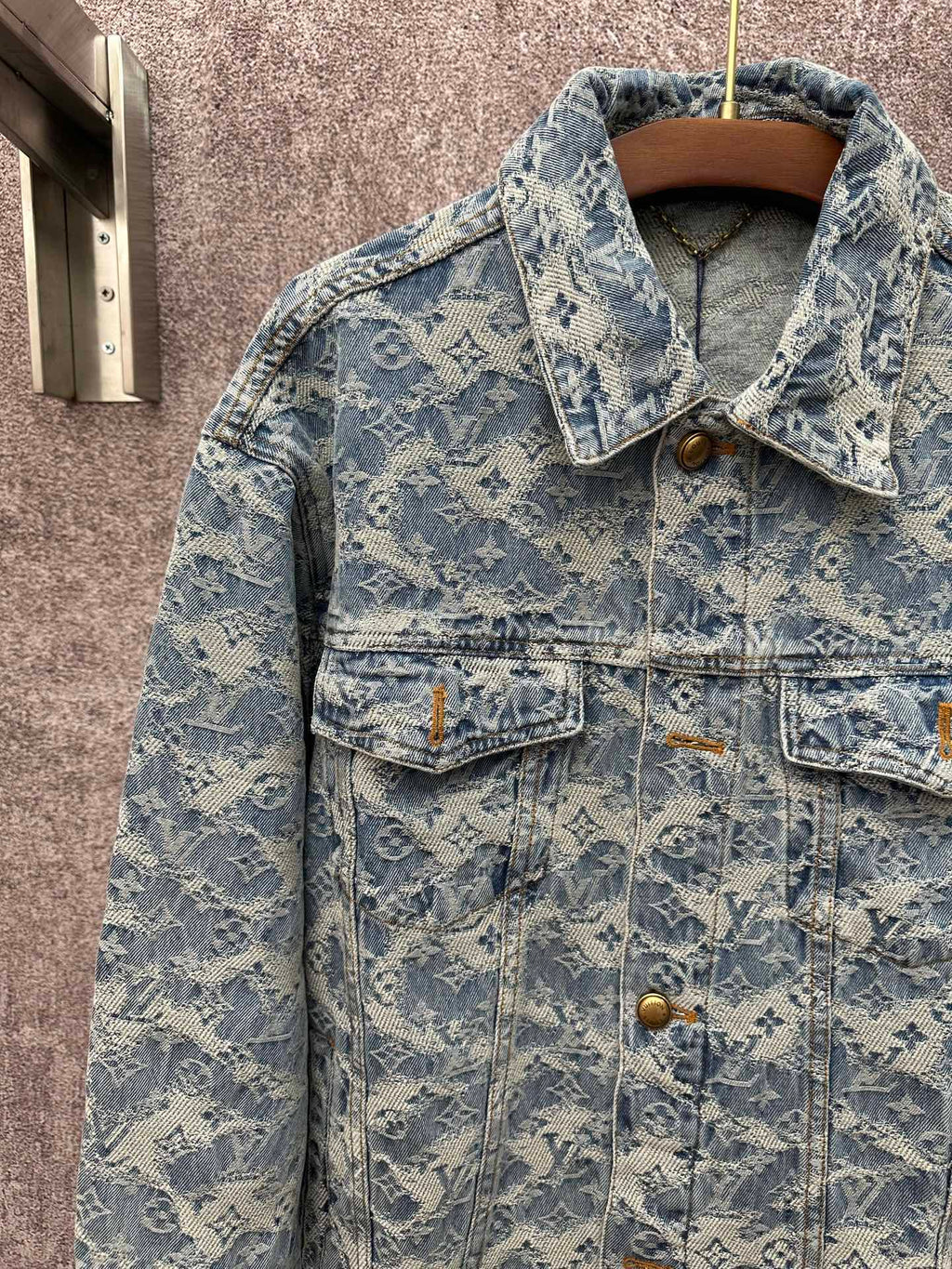 Blue denim jacket close-up with monogram pattern, gold buttons, and flap front pockets