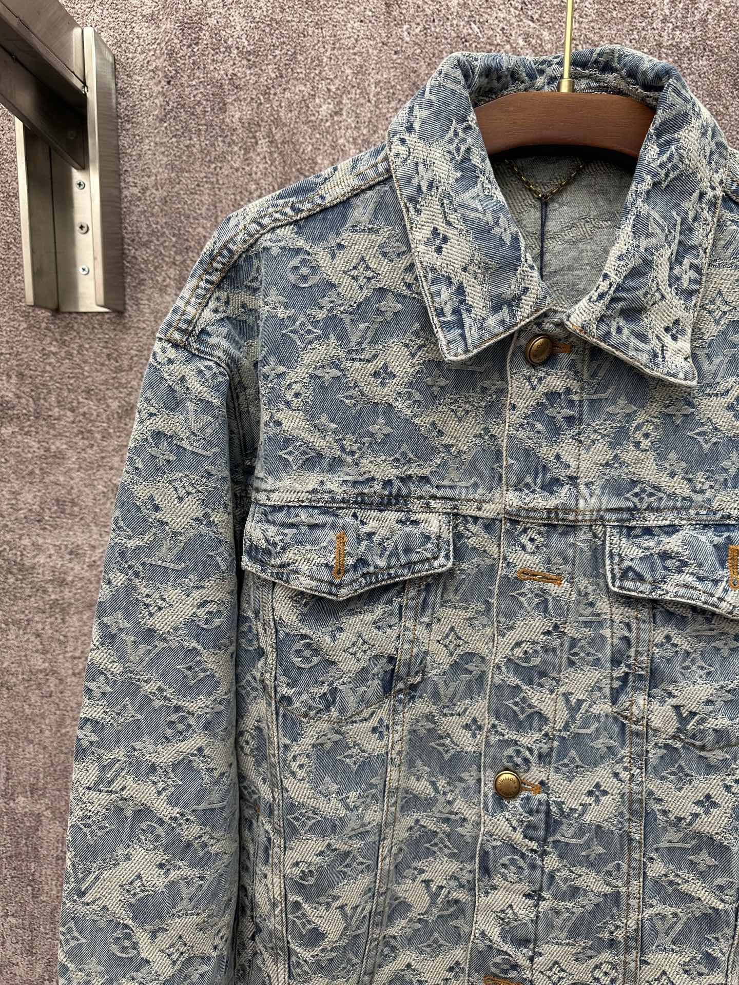 Blue denim jacket close-up with monogram pattern, gold buttons, and flap front pockets