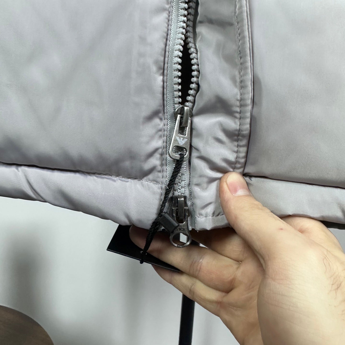 Amiri hooded puffer vest, light gray, close-up of front zipper with metal pull