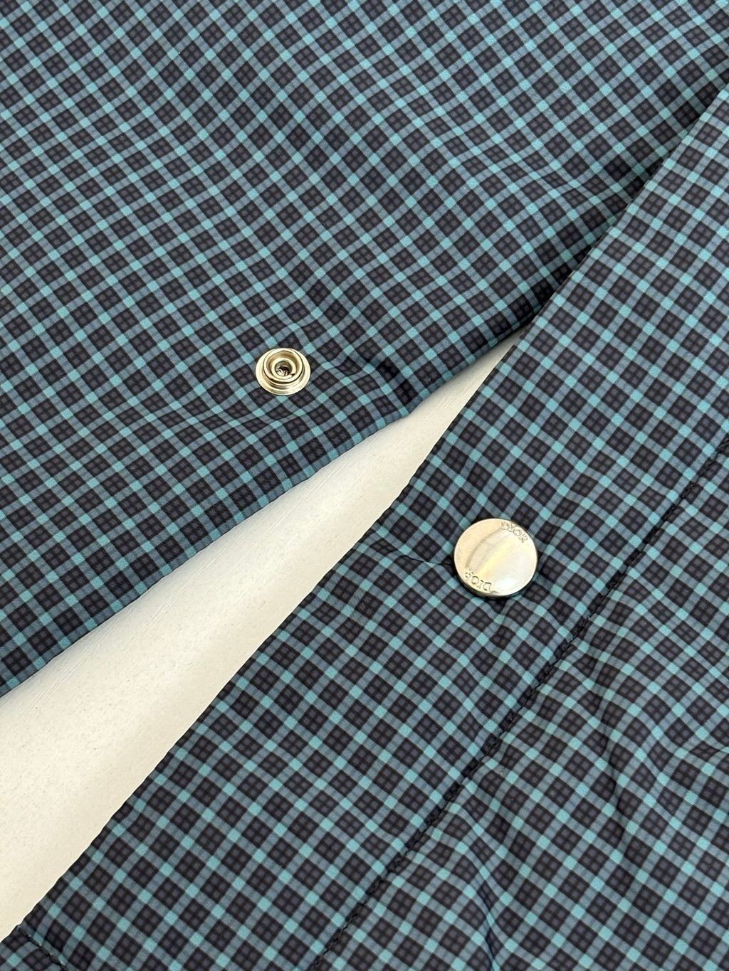 Blue check jacket detail with round button and diagonal seam stitching
