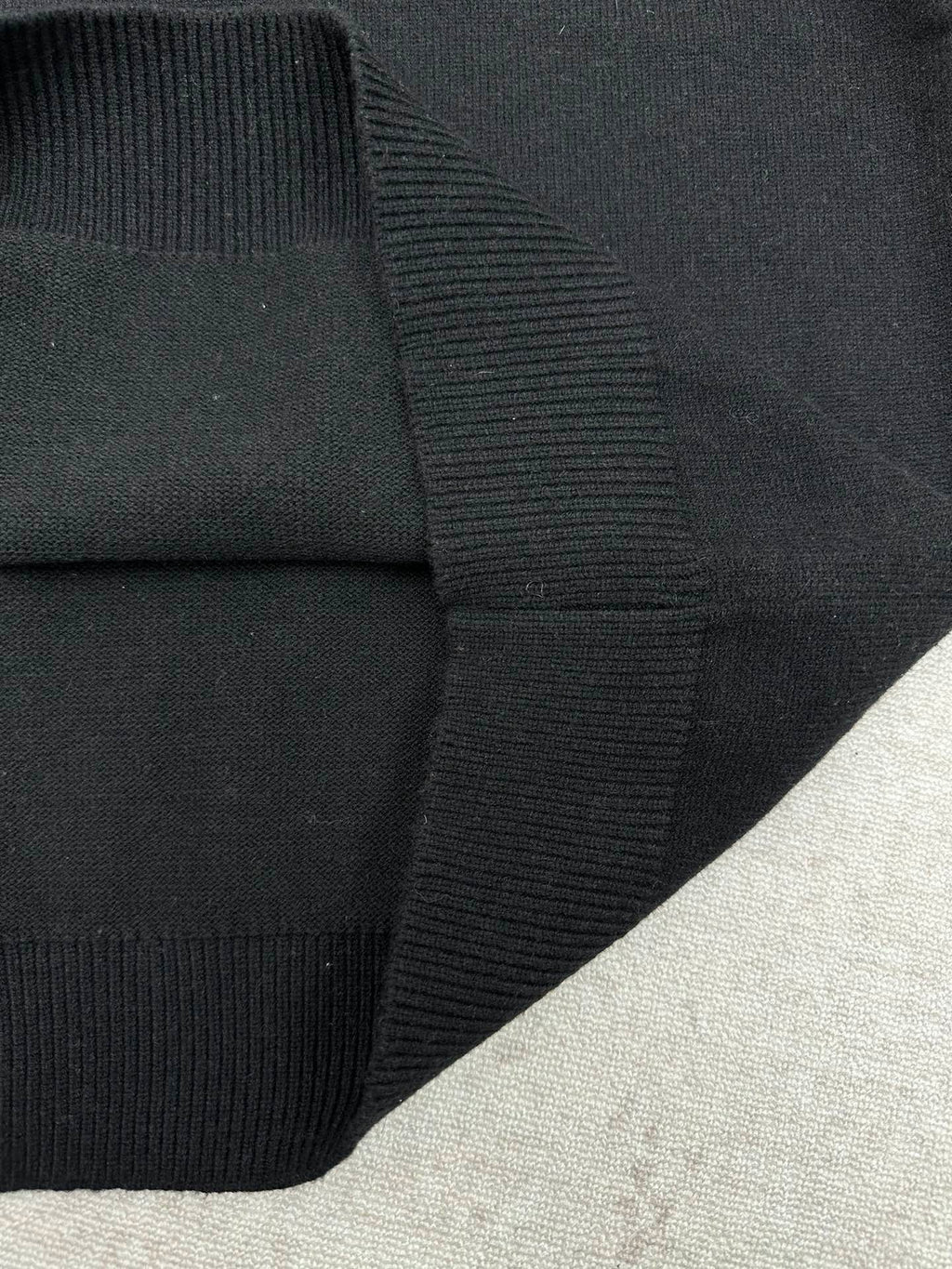 Black sweater cuff with ribbed knit trim at the sleeve hem.