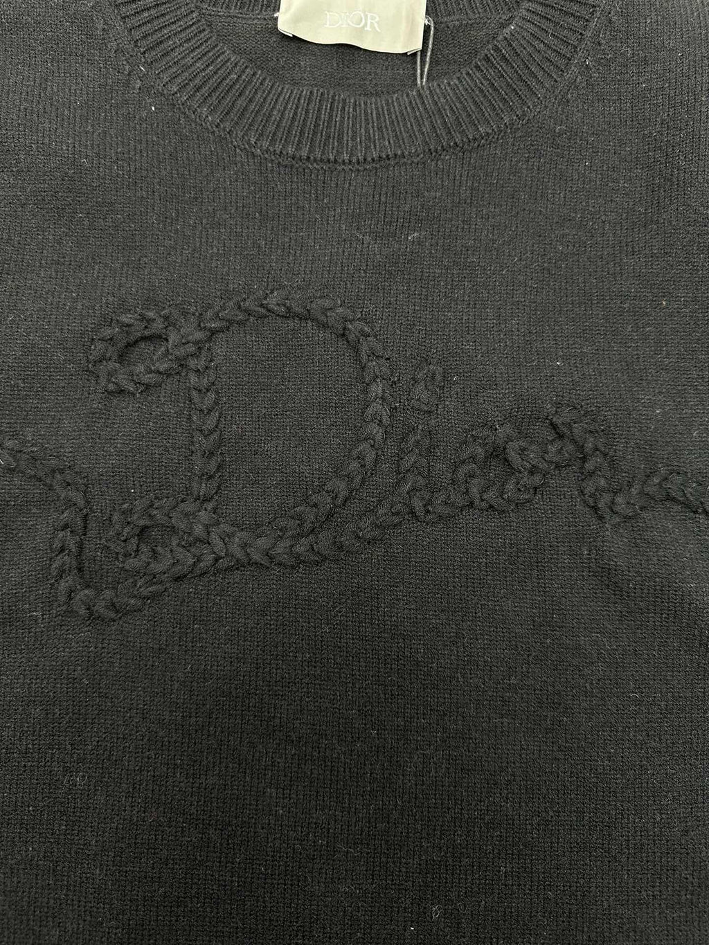 Black knit sweater with embroidered swirl logo detail on the chest.
