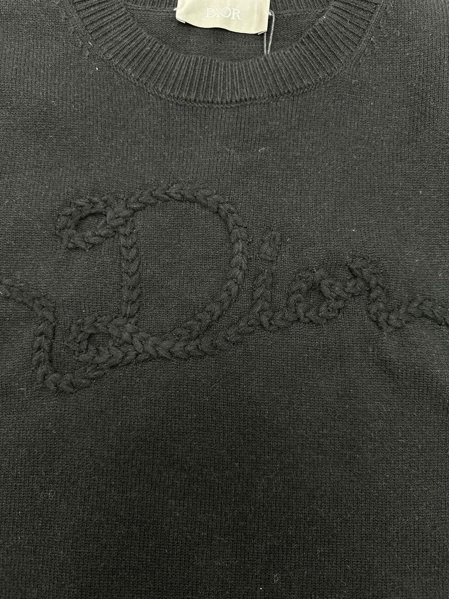 Black knit sweater with embroidered swirl logo detail on the chest.