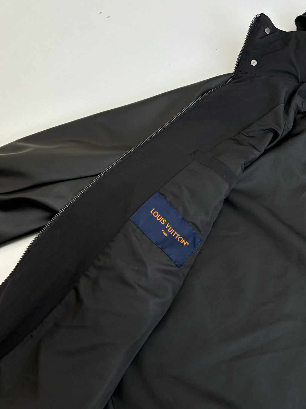 Black jacket with blue Louis Vuitton logo patch on chest and front zipper line.