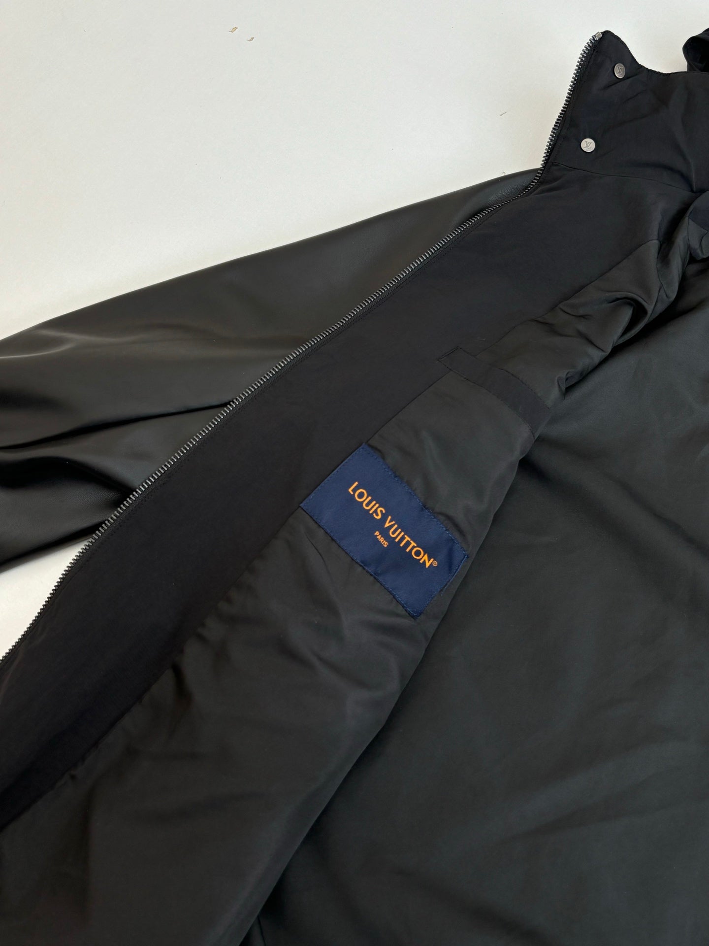 Black jacket with blue Louis Vuitton logo patch on chest and front zipper line.