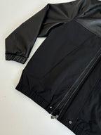Black jacket laid flat with front zipper, ribbed cuffs, and gathered hem.