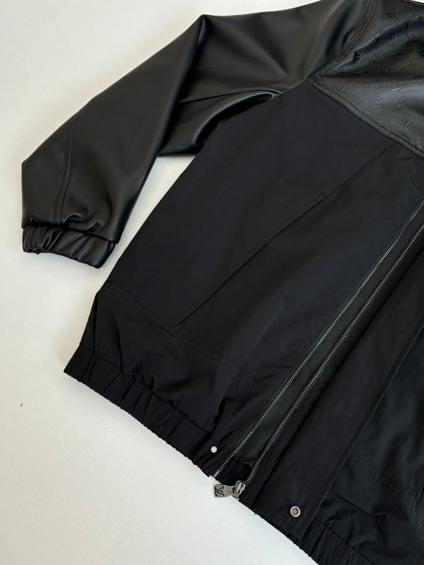 Black jacket laid flat with front zipper, ribbed cuffs, and gathered hem.