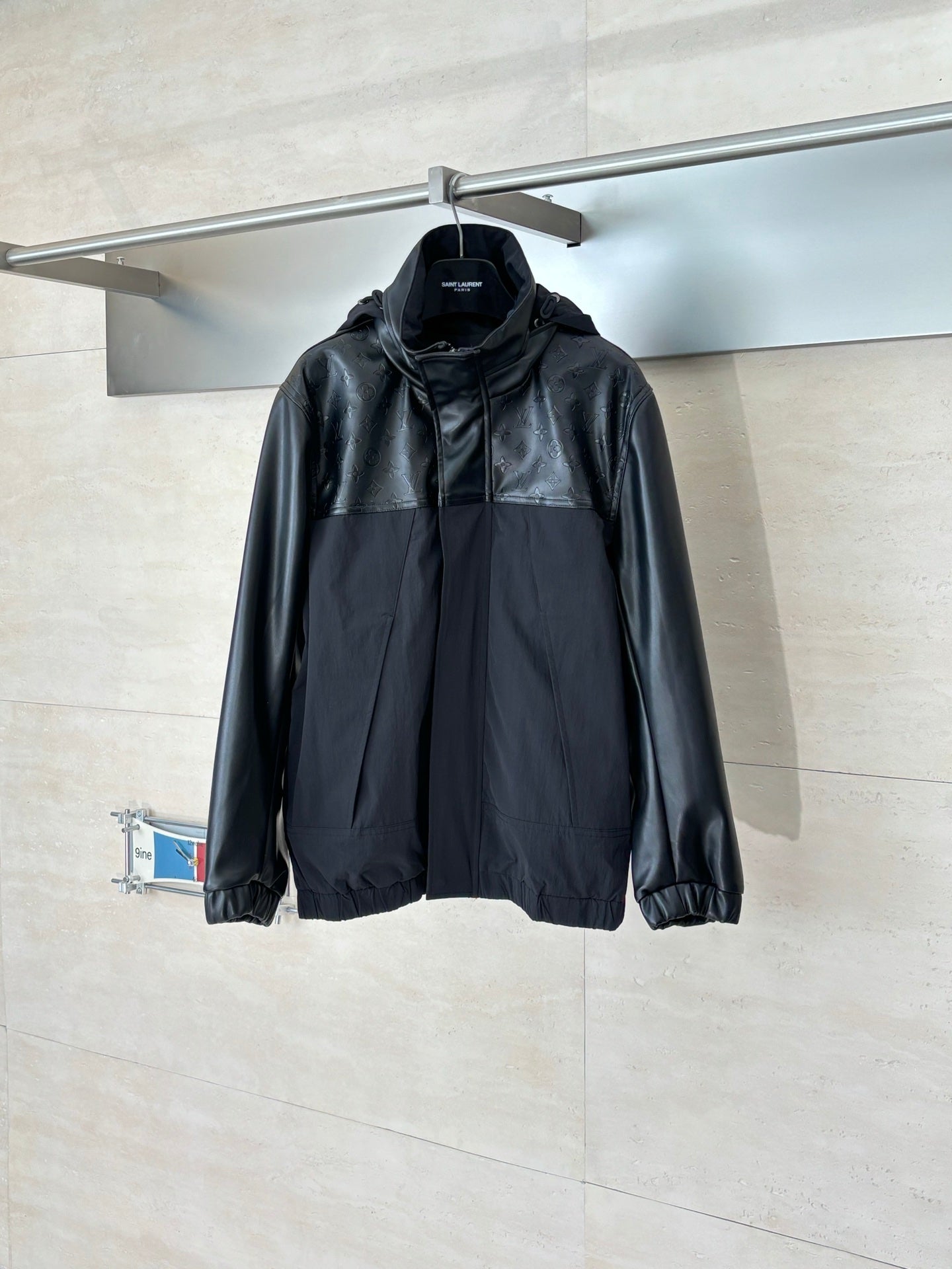 Black hooded zip-up jacket with elastic cuffs and gathered hem, hanging.