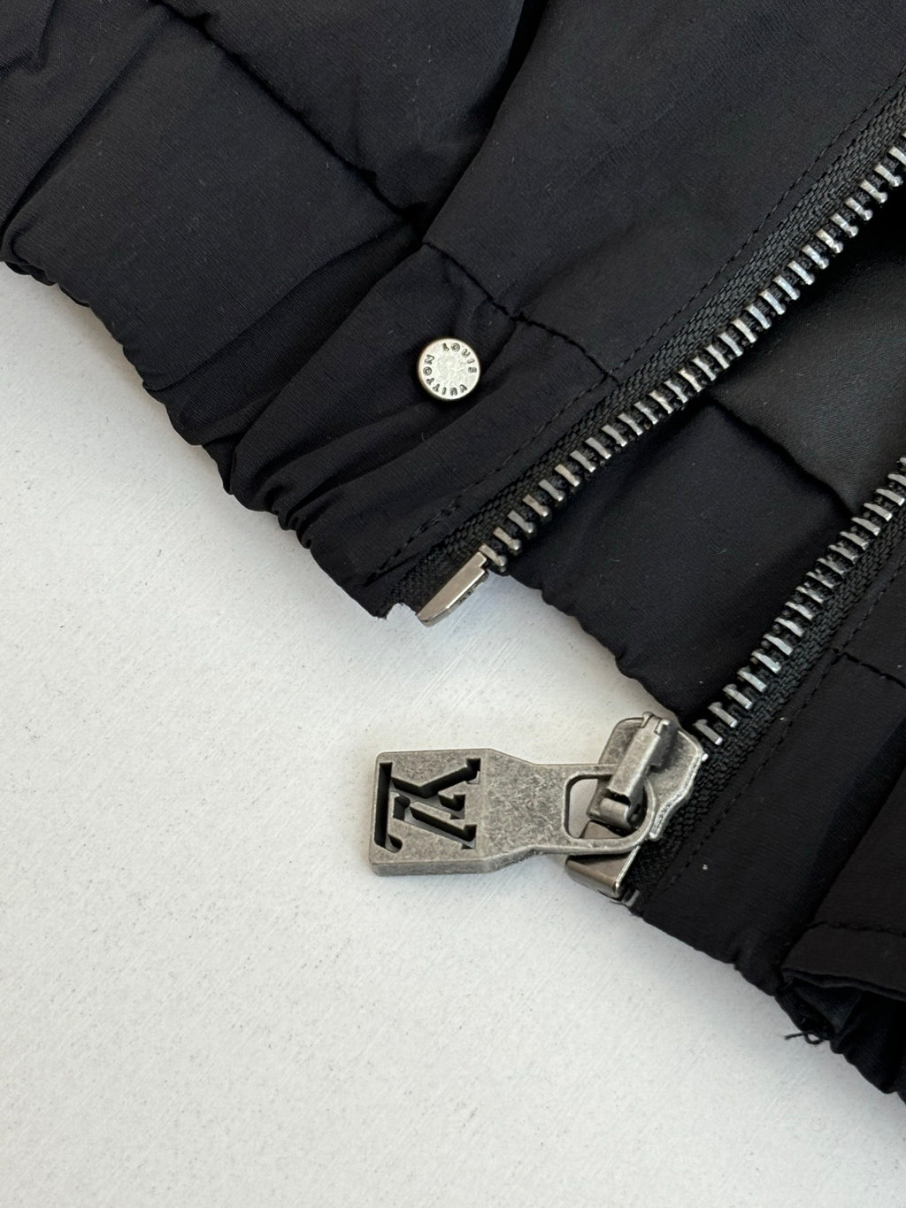 Black jacket cuff detail with round snap button and metal zipper hardware.