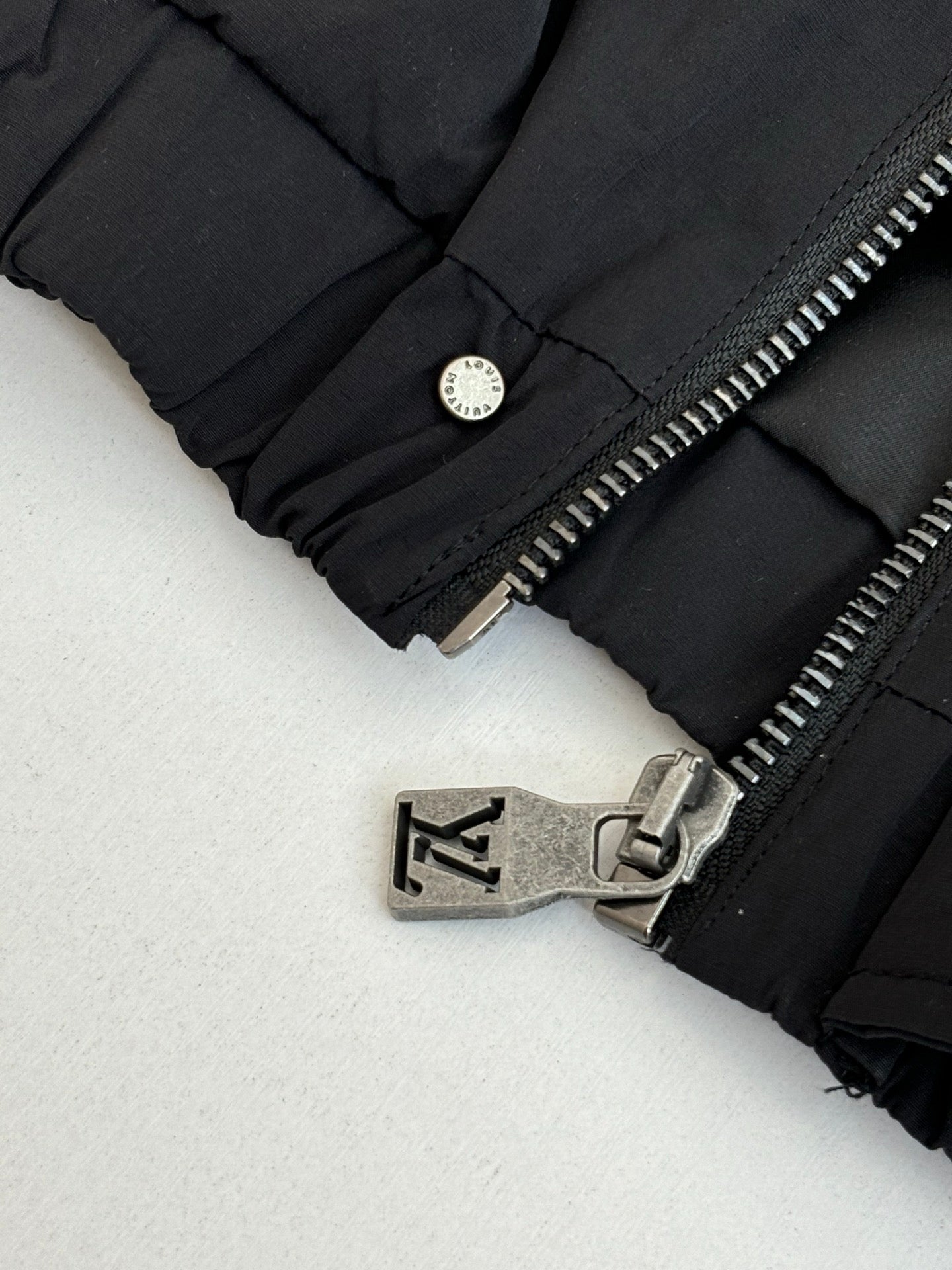 Black jacket cuff detail with round snap button and metal zipper hardware.