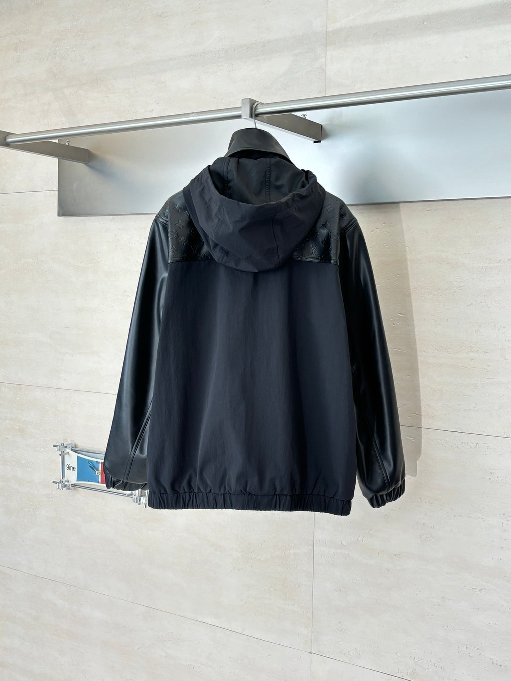 Black hooded jacket with full-zip front and gathered hem, shown from the back.